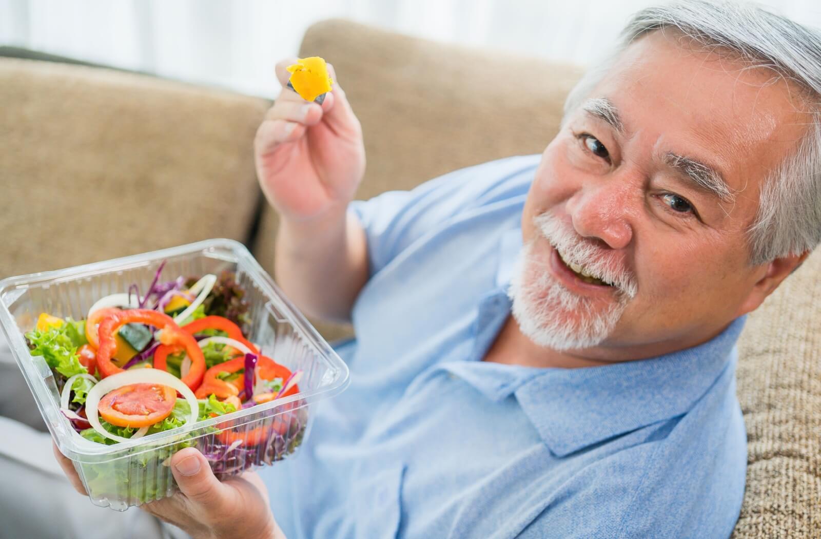 A happy senior man holding a plastic bowl containing salad.