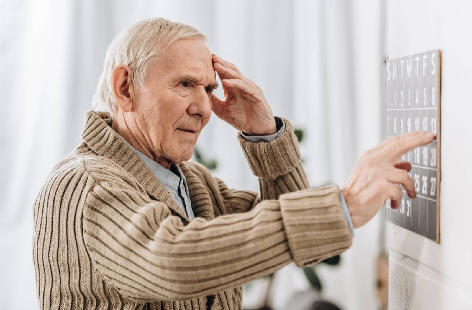 An older adult rubbing their forehead and checking their calendar to test their memory.