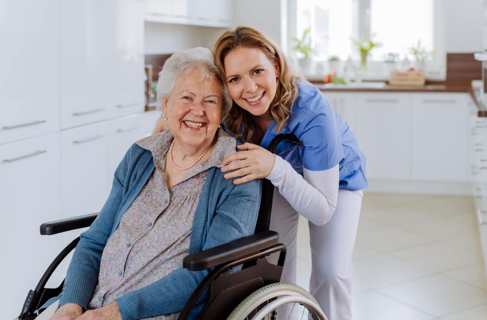 A caregiver hugs an older adult in a wheelchair in assisted living.