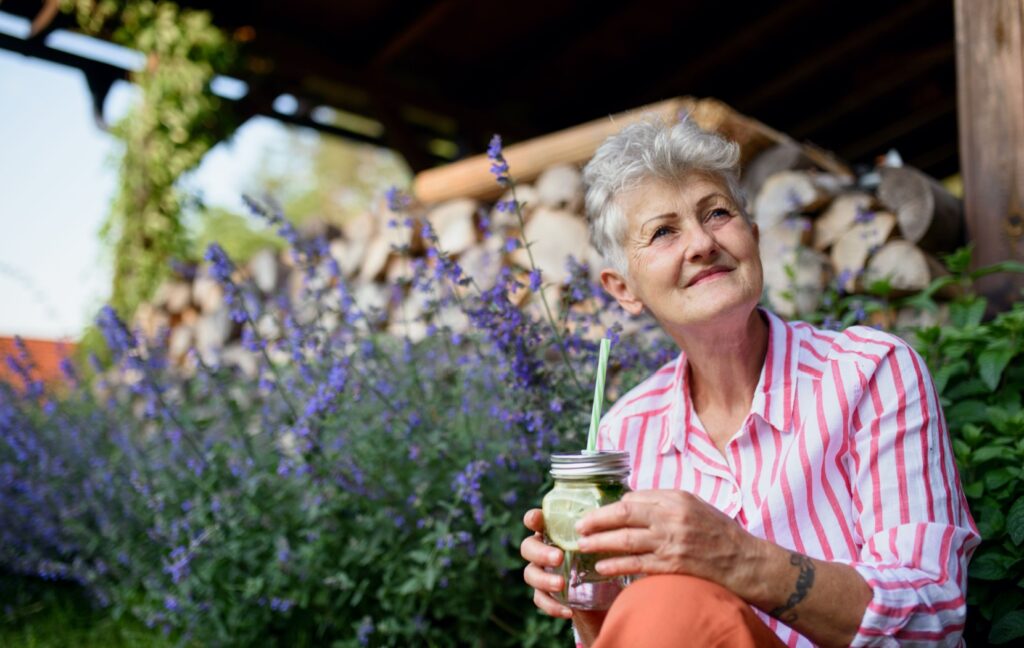 An older adult sitting outdoors and enjoying a refreshing drink in assisted living.