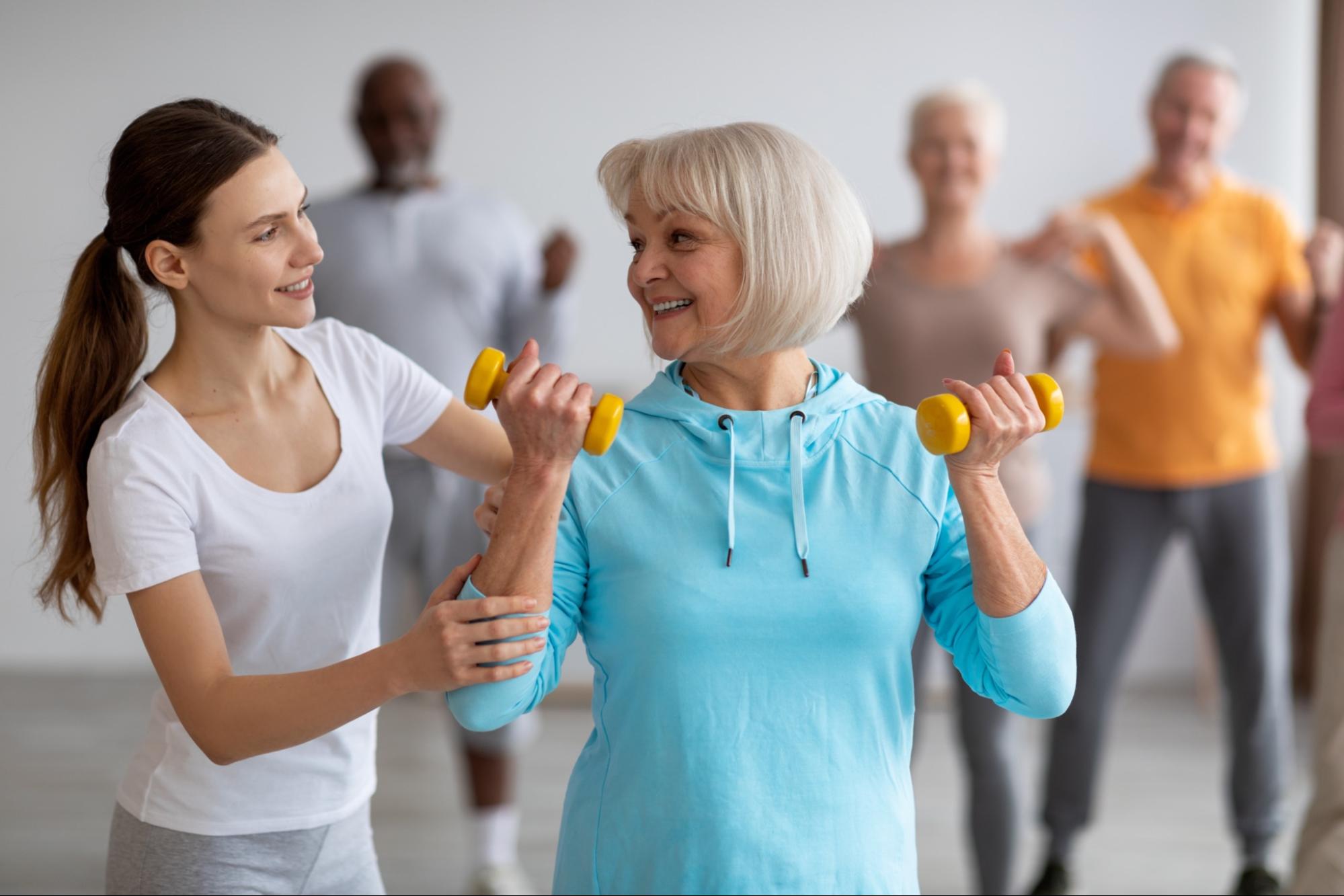 A female fitness coach assisting a group of older adults in an exercise class.