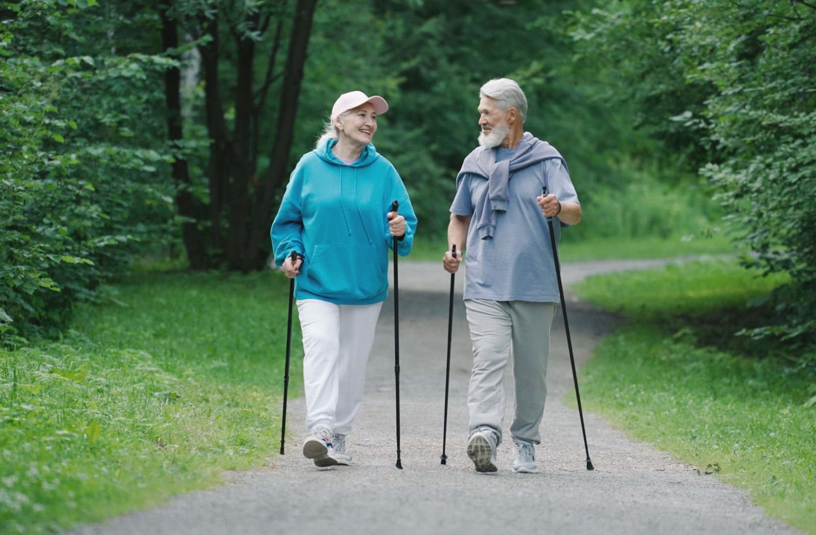Older couple walking with trekking poles on a nature trail for exercise.
