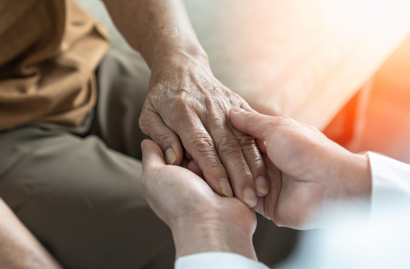 A caregiver holds the hand of an older adult with dementia to reassure them and show support