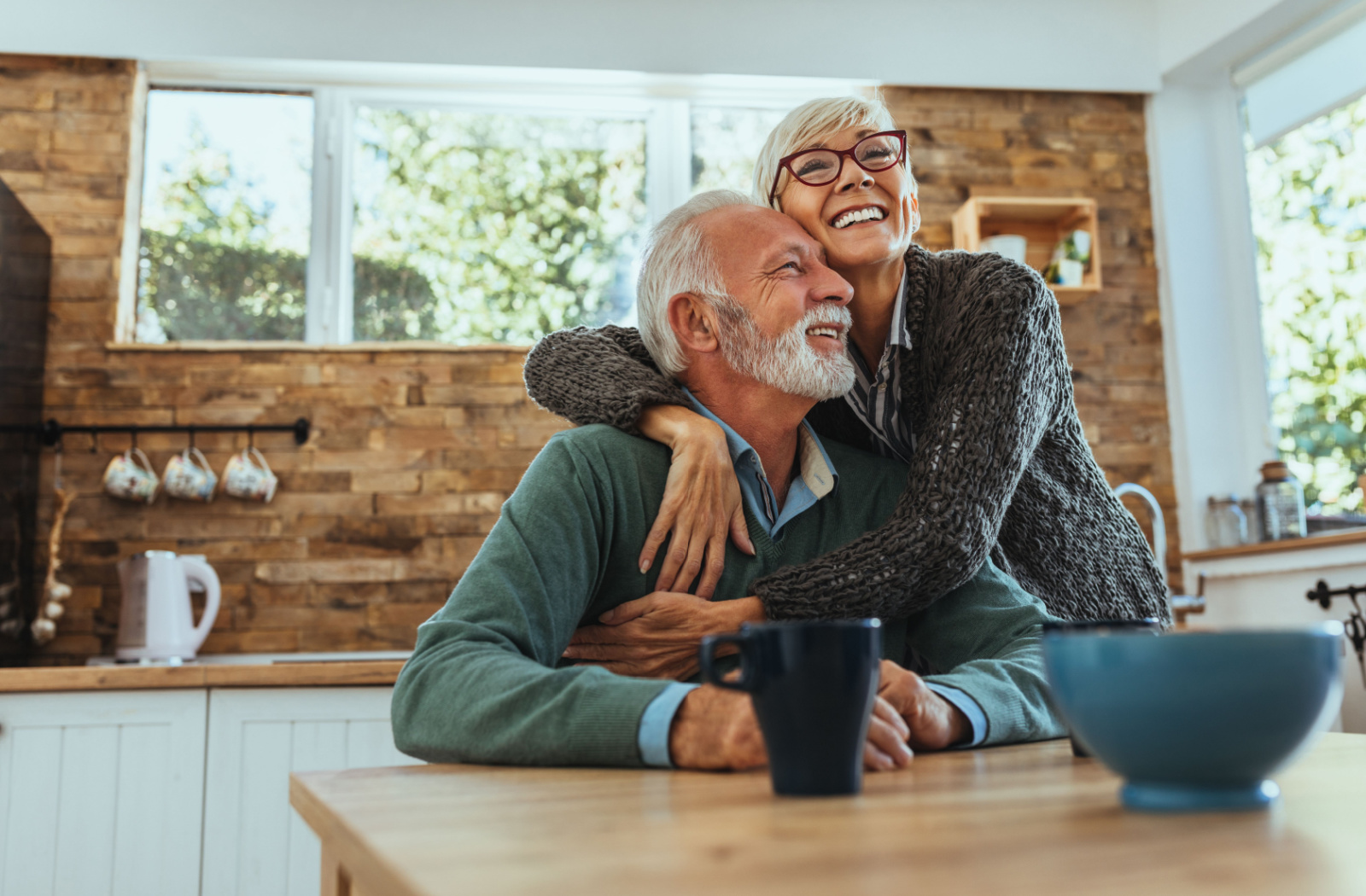 A happy senior woman hugging her happy senior husband.