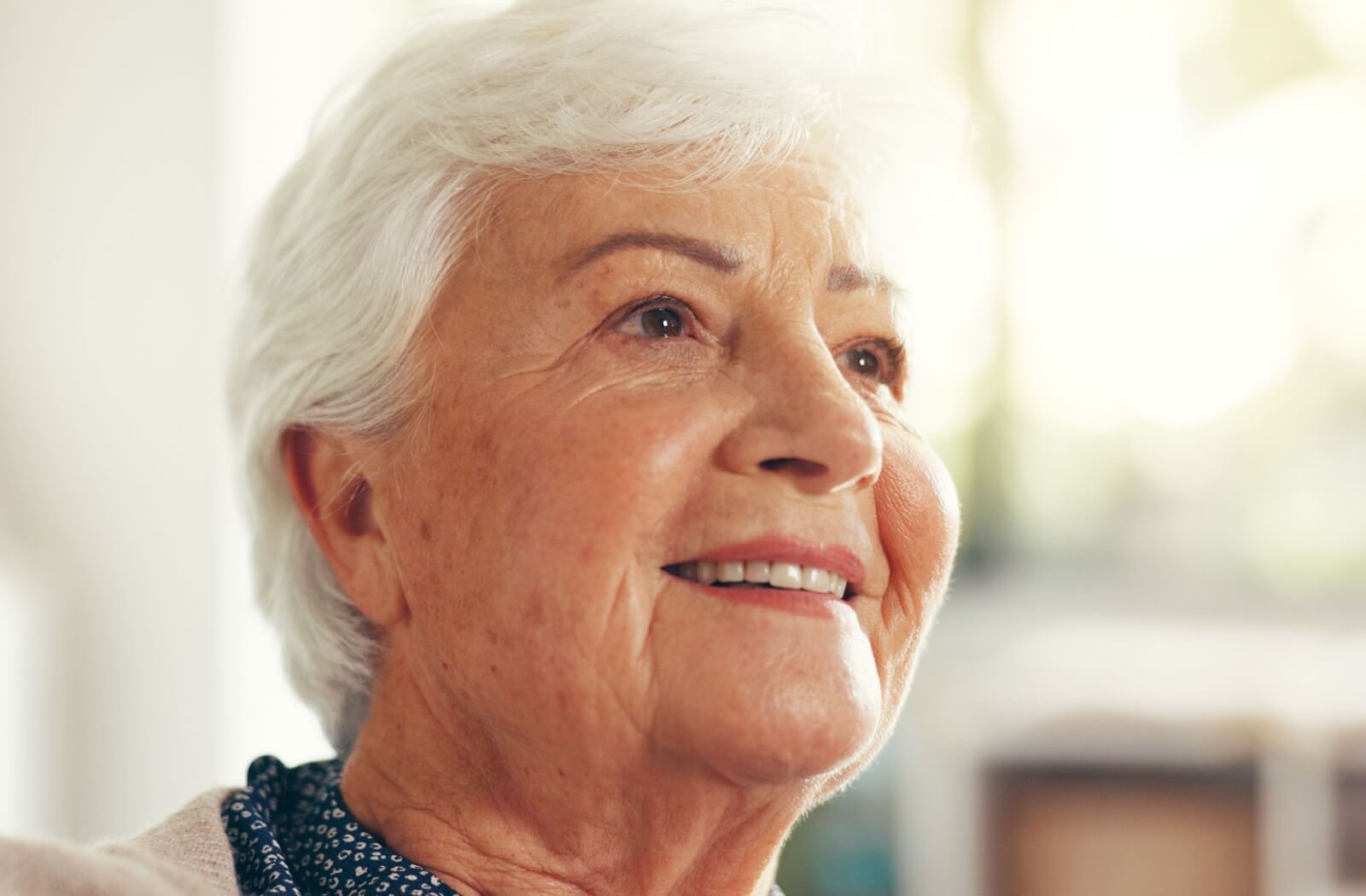 Smiling older adult with white hair looking ahead warmly in natural light creating a sense of comfort and calm at home