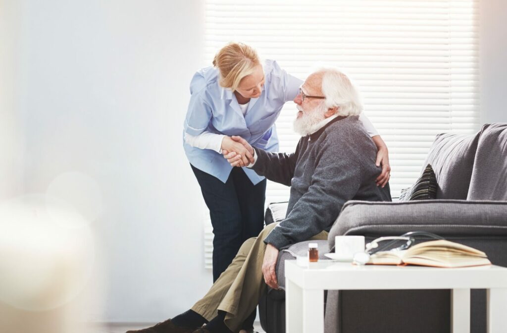 Older adult sitting on couch shaking hands with caregiver offering support and reassurance in a bright comfortable room
