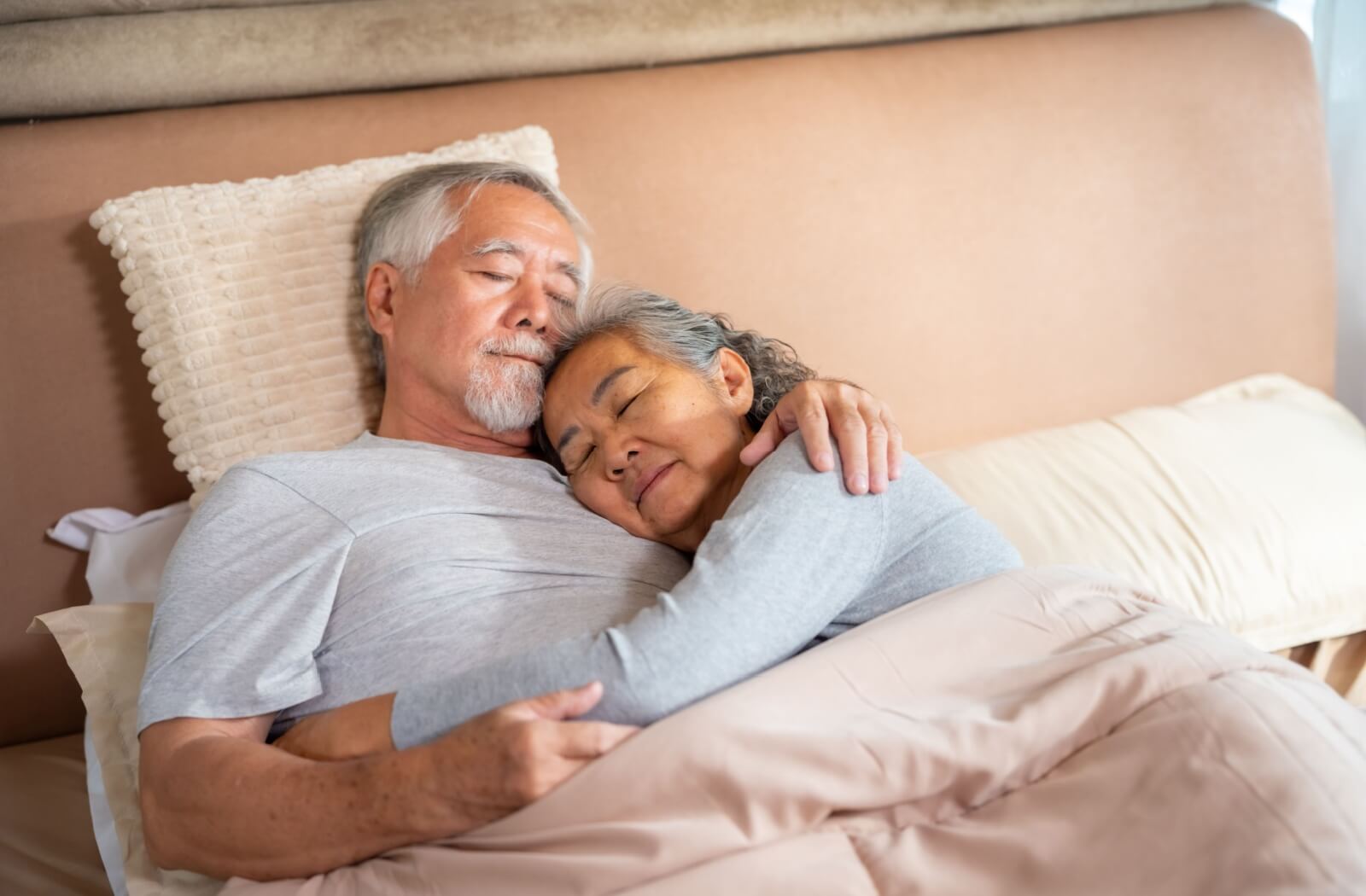 Two older adults cuddle together in bed while sleeping