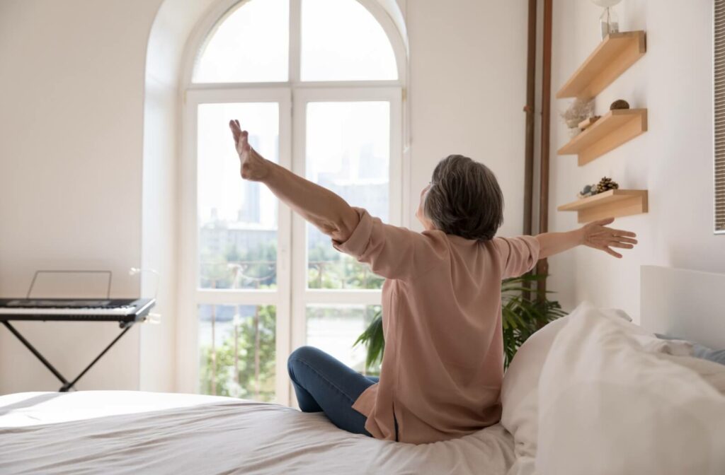 An older adult stretches their arms out, feeling well-rested after waking up in a senior living environment